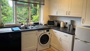 A compact kitchen with a washing machine, a microwave, and a kettle.