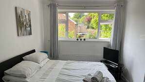 A bedroom with a bed, pillows, a TV, and a window with curtains.
