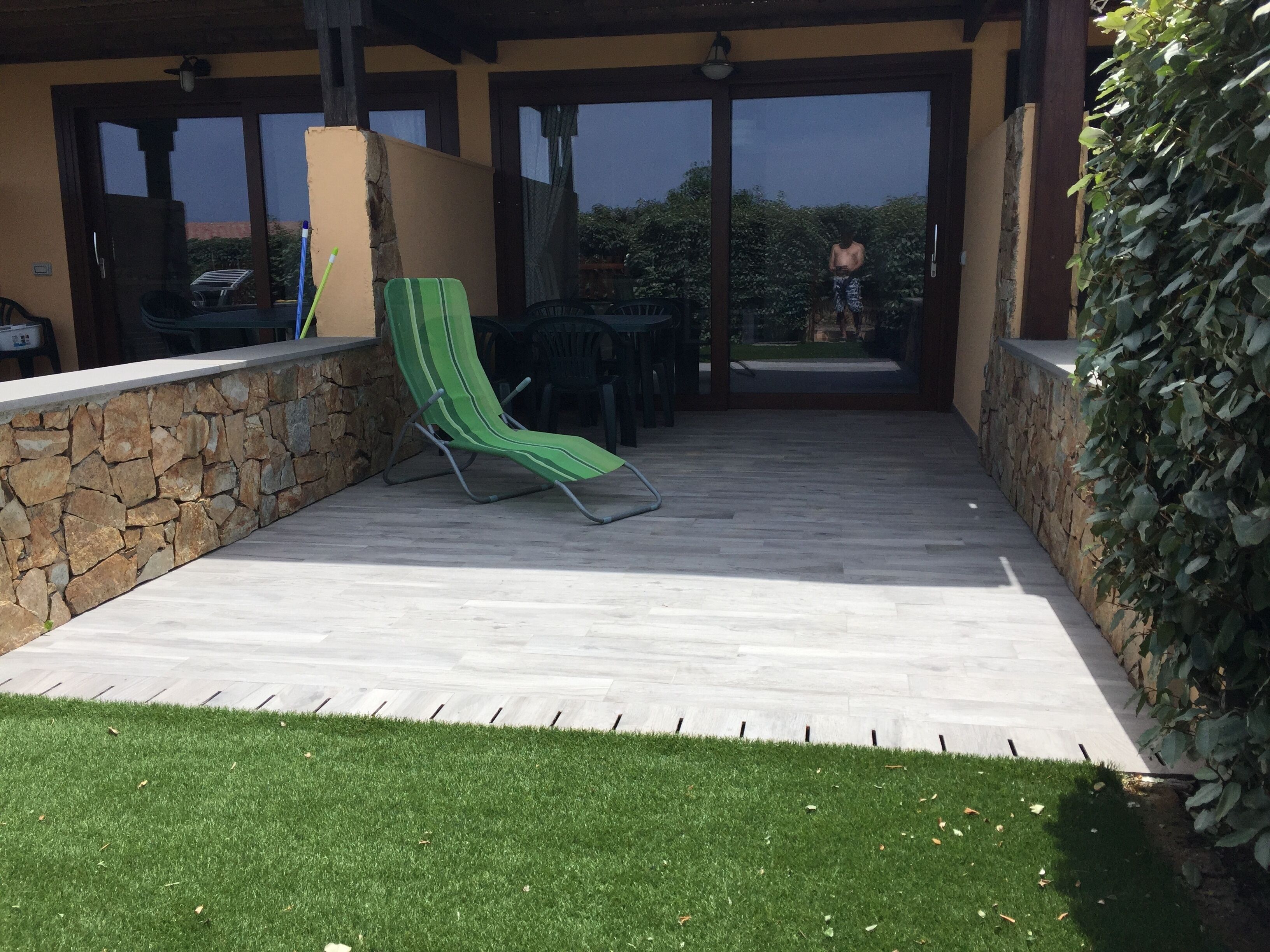 Un patio cubierto con un muro de piedra, un sillón de descanso verde y vistas al exterior.