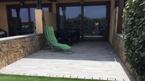 A covered patio area with a stone wall, a green lounge chair, and a view of the outdoors. - Palau (OT), 650 meters from the beach, ideal for couples and families (PALAU (OT))