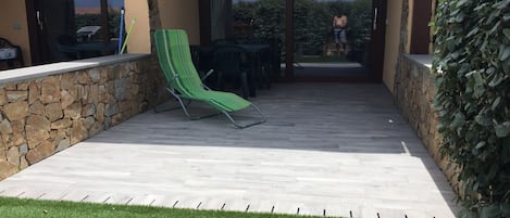 Een overdekt terras met een stenen muur, een groene lounge stoel en uitzicht op de omgeving.