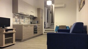 A modern living room with a flat-screen TV, a blue sofa, and a kitchen area with a microwave and oven. - Palau (OT), 650 meters from the beach, ideal for couples and families (PALAU (OT))