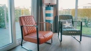 Una sala de estar moderna con dos sillones de cuero, una lámpara de pie a rayas y vistas a un jardín a través de amplios ventanales.