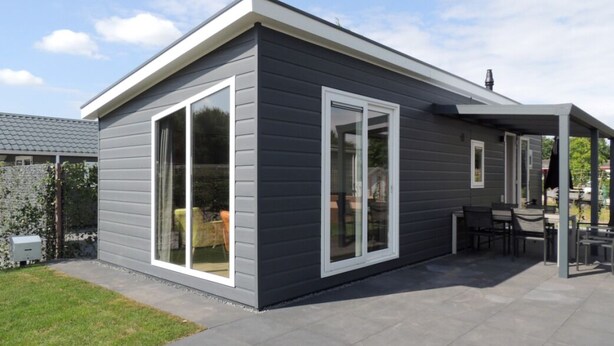 Una casa moderna con un patio, amplias puertas correderas de vidrio y un área de estar cubierta al aire libre.