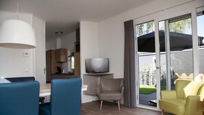 Una sala de estar moderna con comedor, televisor y puerta corrediza de vidrio que da a un jardín.