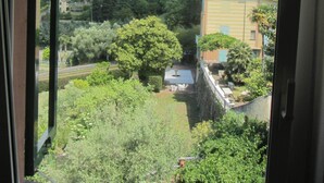 Blick durch ein Fenster auf eine Wohngegend mit einem Hügel im Hintergrund, eine Straße und etwas Grün.