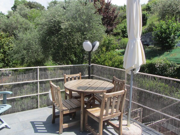 A wooden table and chairs on an outdoor patio with a view of greenery.