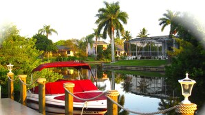 A boat docked at a marina with a red canopy, surrounded by lush greenery and palm trees. - VILLA SUNSET KISS•SW•DREAMLESS BEAUTIFUL•CHANNEL CROSSING WITH SEA ACCESS ***** (Cape Coral)