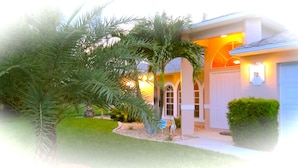 A house with a well-maintained lawn, a palm tree, and a garage. - VILLA SUNSET KISS•SW•DREAMLESS BEAUTIFUL•CHANNEL CROSSING WITH SEA ACCESS ***** (Cape Coral)