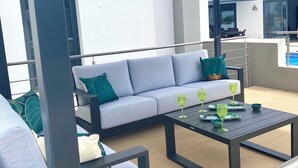 A covered outdoor seating area with a sofa and two tables, one with glasses. - Amazing 2 bed villa, private pool, close to beach/restaurants/bars/golf/tennis (Carvoeiro)