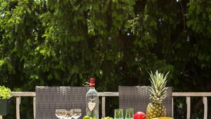 Et bord dækket udendørs med en flaske, glas, frugt og en ananas.