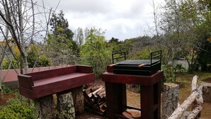 A barbecue grill setup with a wooden bench and a stone pathway. - Rural Tourism - Laurissilva Forest (Camacha)