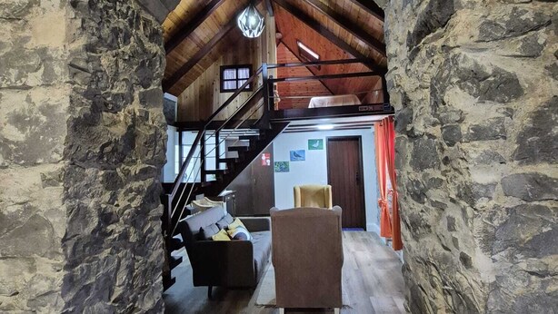 A stone-walled room with a wooden staircase leading to a loft area. - Rural Tourism - Laurissilva Forest (Camacha)