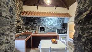 A rustic kitchen with a stone wall, a tiled ceiling, and a built-in oven. - Rural Tourism - Laurissilva Forest (Camacha)