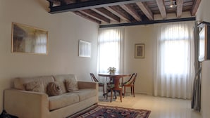 Una sala de estar con un sofá, una mesa de comedor con sillas y un techo con vigas a la vista.