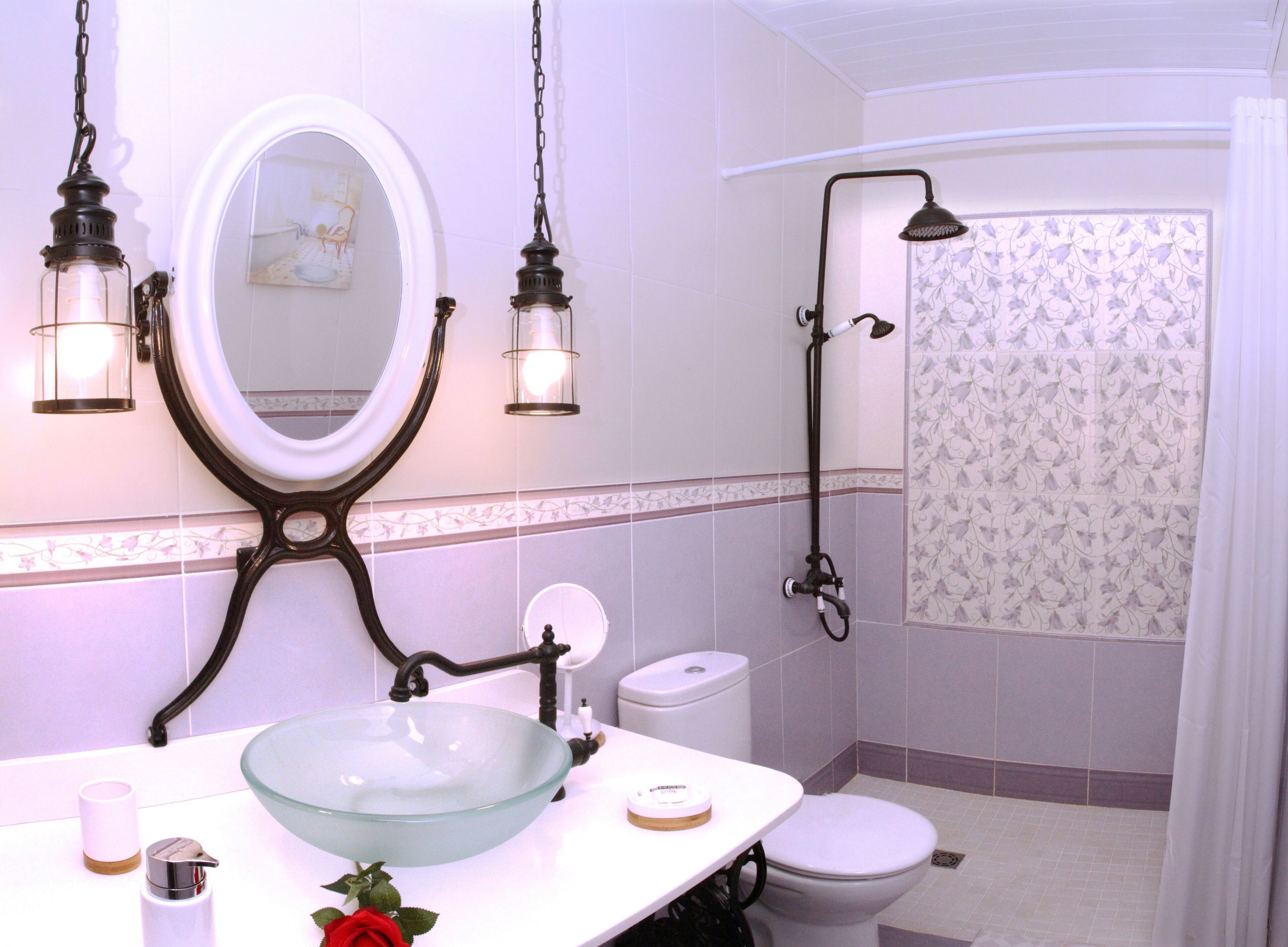 Een badkamer met een wasbak van glas, een wit toilet, een douche met gordijn en twee wandlampen.
