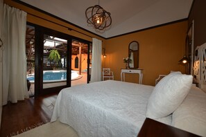 Ein Schlafzimmer mit einem großen Bett, einem kleinen Tisch, einem Sessel und Blick auf einen Pool und Außenbereich.