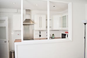 A modern kitchen with white cabinets, a stainless steel range hood, and a microwave.