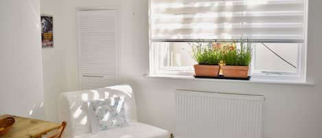 Een kamer met een radiator, een raam met zonwering, een tafel met stoelen en een kamerplant op de vensterbank.