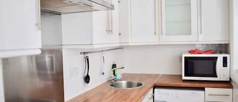 A modern kitchen with white cabinets, a stainless steel sink, a microwave, a built-in oven, and a washing machine.