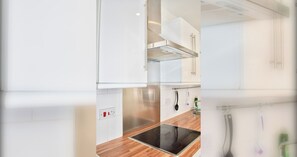 A modern kitchen with white cabinetry, a stainless steel range hood, and a black induction cooktop.