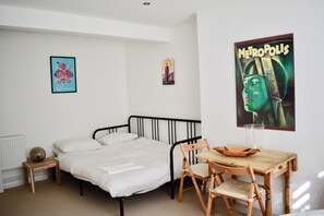 Un dormitorio con una cama individual, una silla de madera, una mesita y un cartel en la pared.