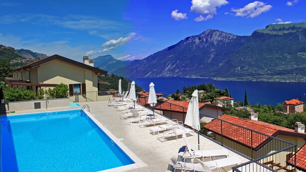 Area piscina con lettini e vista su un lago e montagne.