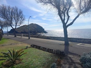 Stroll along the coastal promenade with a breathtaking view of the sea and a hill in the background.