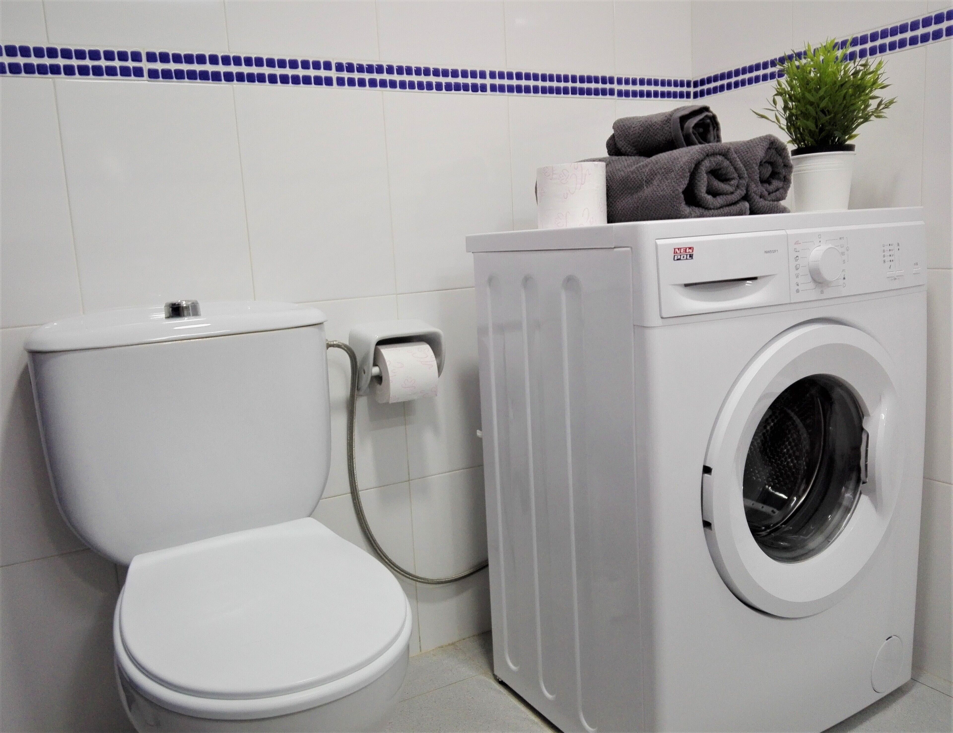 A bathroom with a toilet, a washing machine, and a toilet paper holder.
