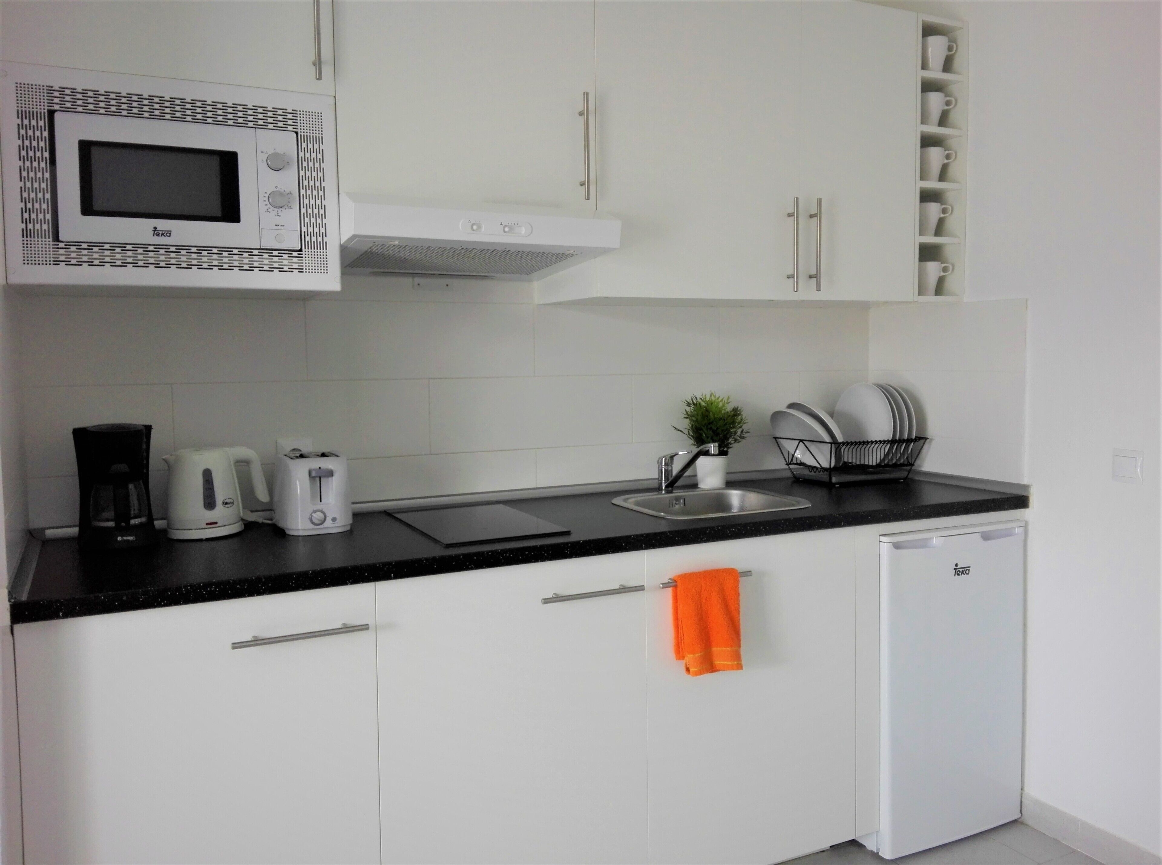 A modern kitchen with white cabinets, a microwave, a coffee maker, a toaster, a sink, and a dish rack.