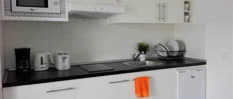 A modern kitchen with white cabinets, a microwave, a coffee maker, a toaster, a sink, and a dish rack.