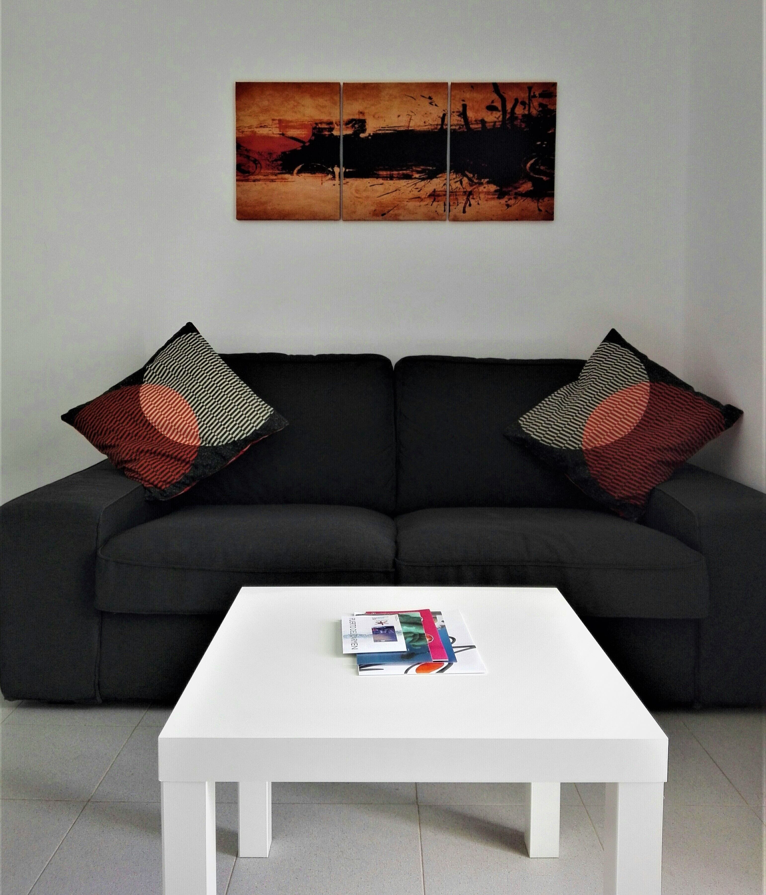 Een moderne woonkamer met een zwart hoekbank, twee decoratieve kussens met prints en een witte salontafel met tijdschriften.