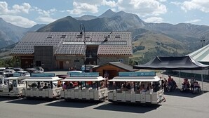 Un espace de stationnement où sont garés plusieurs petits véhicules blancs, ouverts sur le dessus, probablement utilisés pour le transport de touristes, devant un bâtiment doté d’un toit en tuiles et d’une enseigne indiquant la présence d’un restaurant.