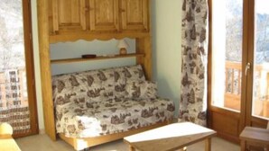 Une pièce chaleureuse avec un meuble en bois, un canapé à motifs, une petite table et une vue sur l’extérieur, visible à travers une porte vitrée.