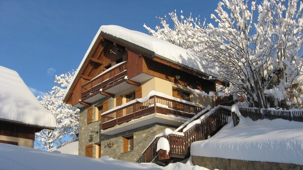 Un chalet en bois à plusieurs étages, doté de balcons et entouré d’arbres couverts de neige.