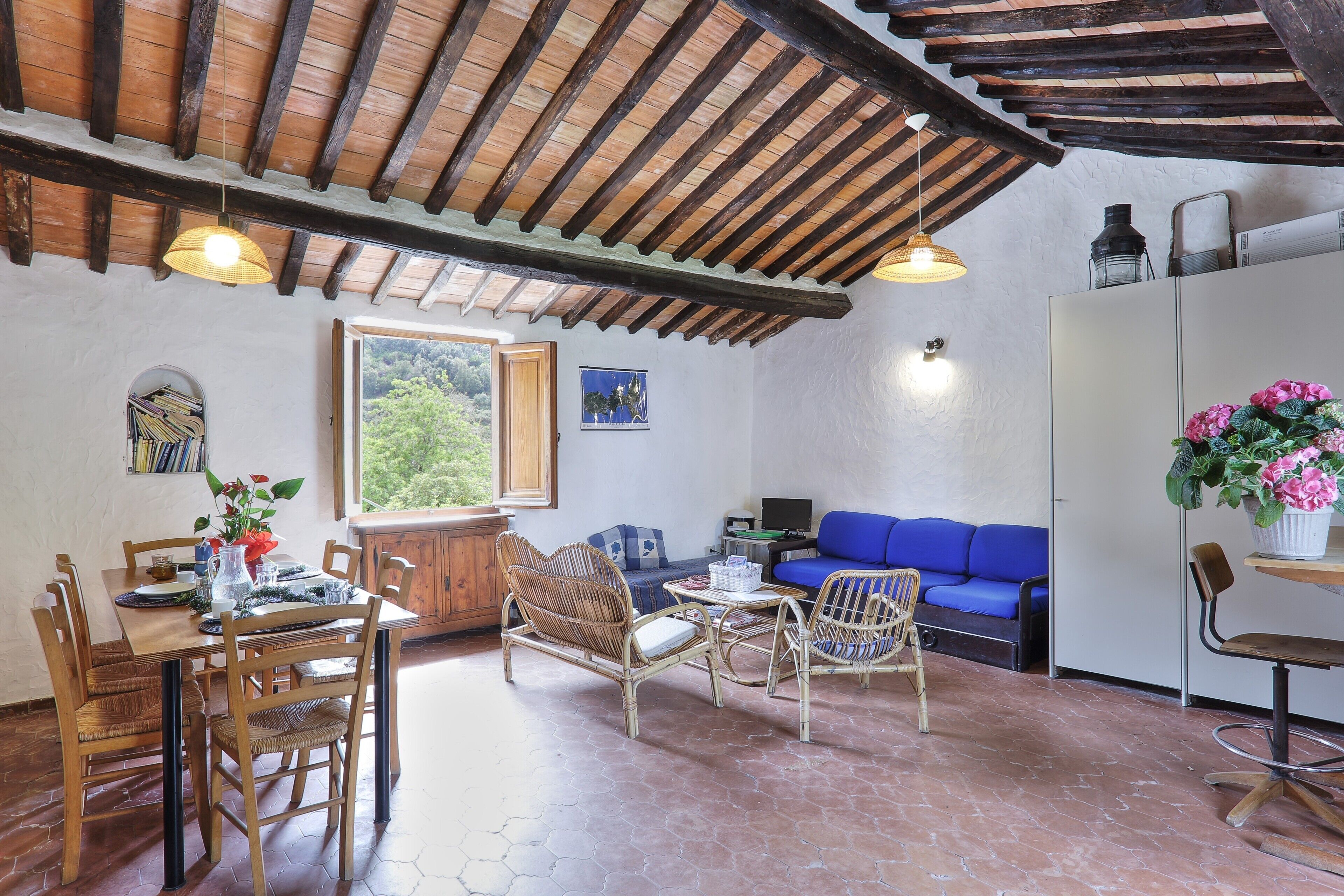 Un intérieur rustique avec une table à manger en bois, des chaises en osier, un canapé bleu et un sol carrelé.