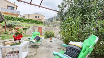 Un patio con dos sillones verdes, una mesa blanca con un florero y una mesita con una bandeja y tazas.