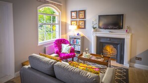 Ein Wohnzimmer mit Kamin, einer Couch, einem Sessel, einem Bücherregal und einem Fernseher.