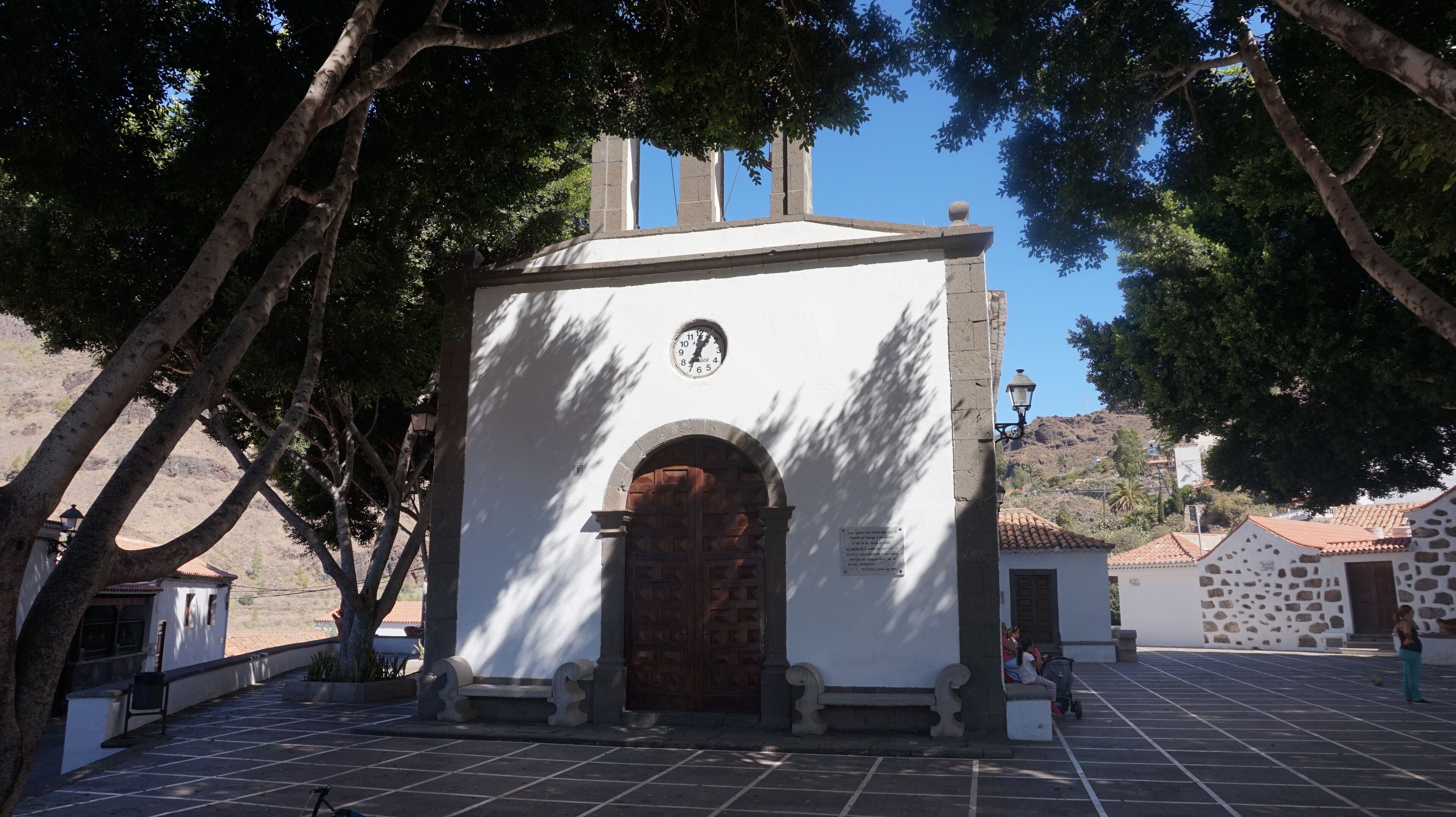 A small white building with a clock, a wooden door, and a bench.
