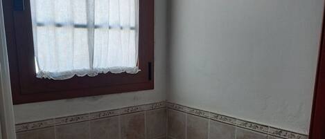 Une petite salle de bain avec des toilettes, une fenêtre ornée d’un rideau en dentelle et un élément décoratif en bois accroché au mur.