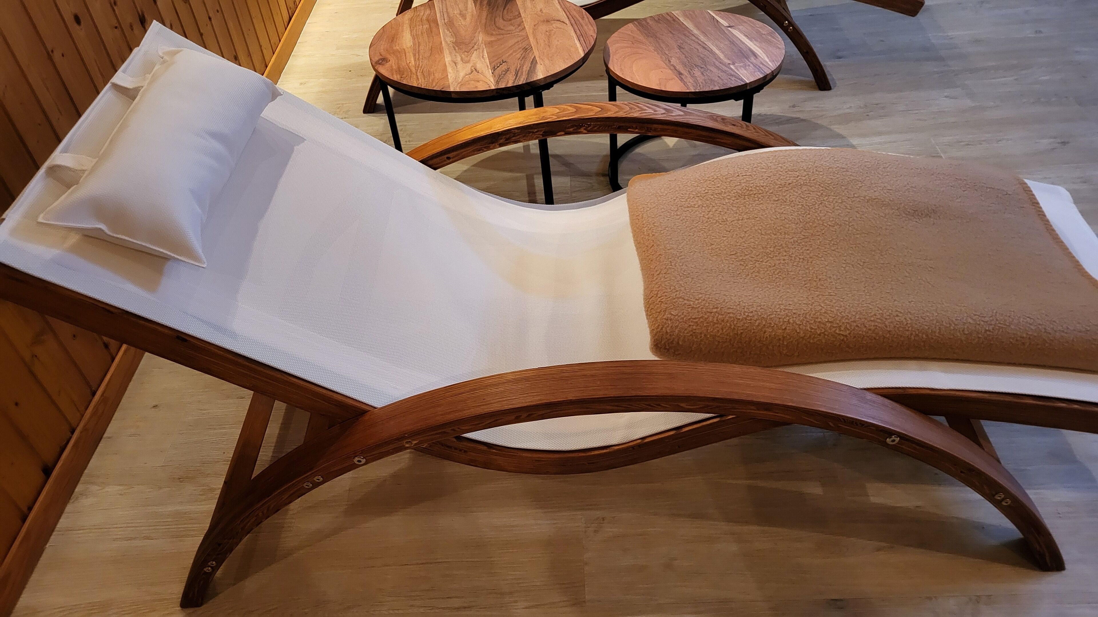 A modern lounge chair with a white cushion and a brown cushion, placed on a wooden floor with a wooden wall in the background.