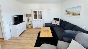 Ein modernes Wohnzimmer mit einem dunkelgrauen Sofa, einem Holztisch, einem weißen Schrank, einem Fernseher und einer Lampe.