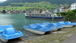 A row of small blue boats tied to a dock with a larger blue and white boat in the background.