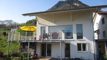 A two-story house with a balcony, a yellow umbrella, and a mountain in the background.