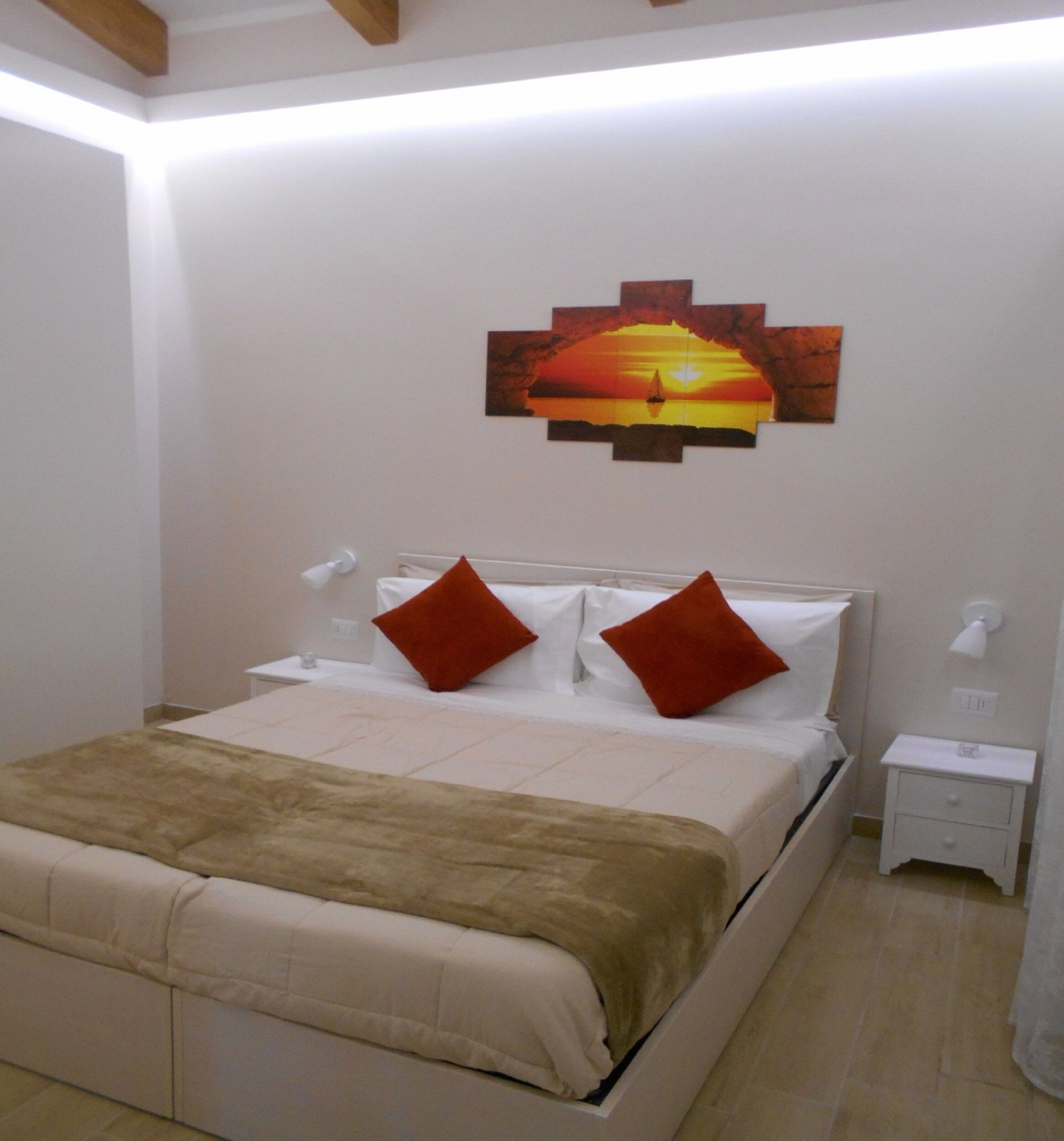 Un dormitorio ordenado con cama, dos mesitas de noche y una obra de arte en la pared que representa un atardecer.