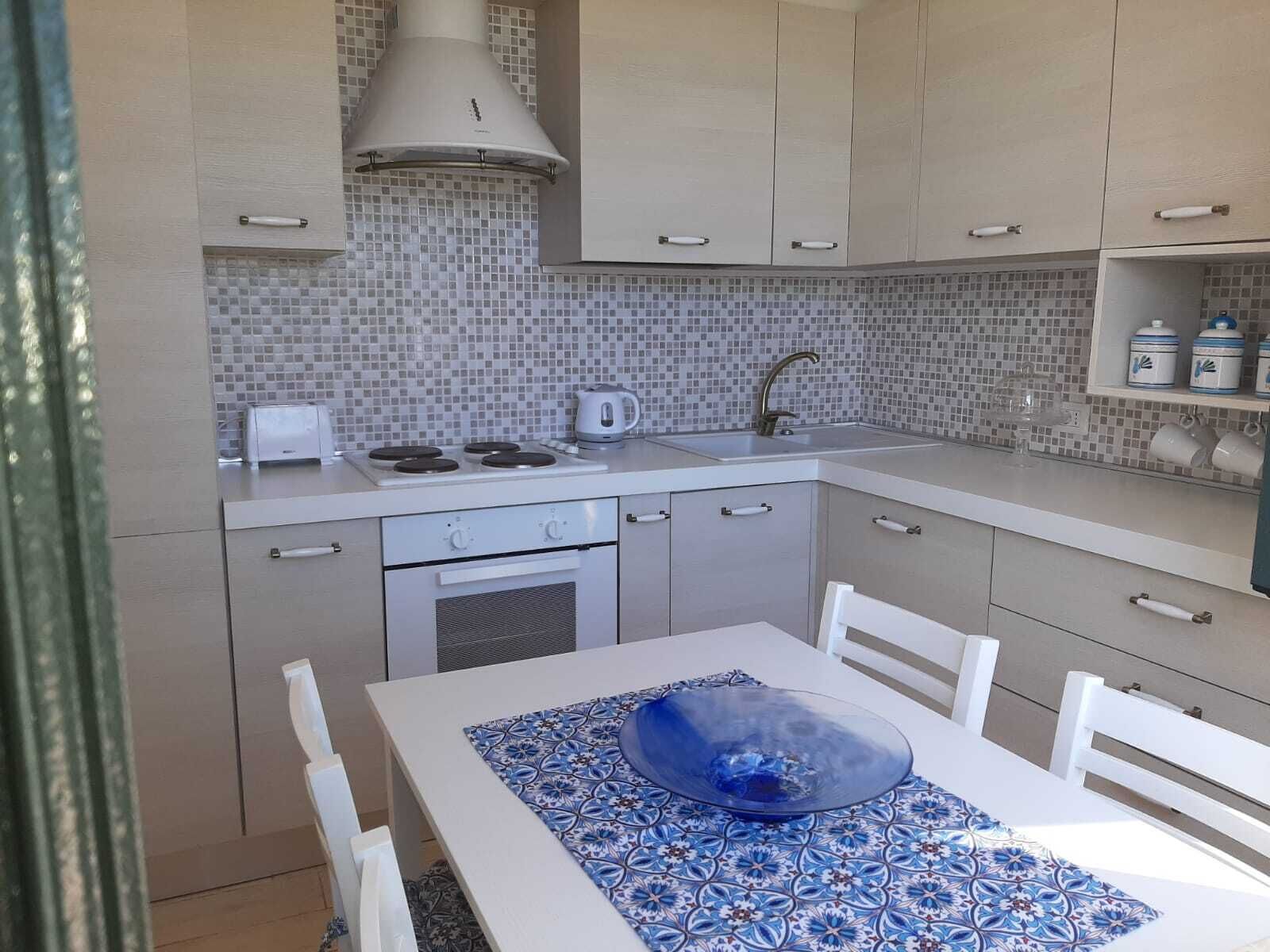 A compact kitchen with a tiled backsplash, a stove, a sink, and a dining table with chairs.