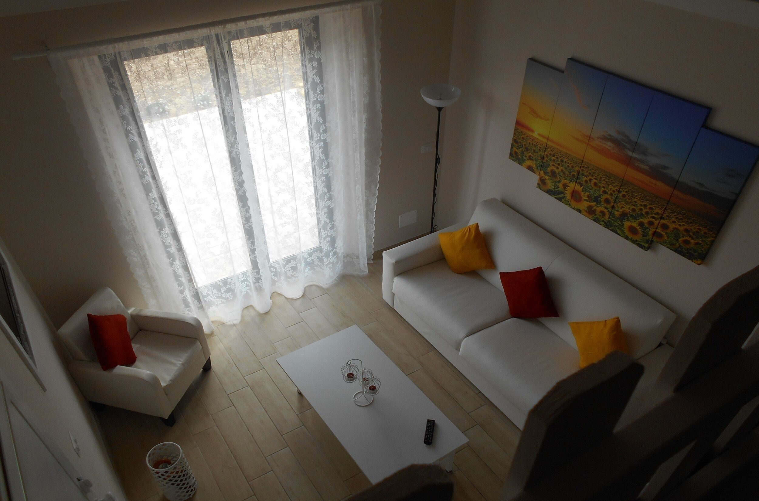 Een woonkamer met een witte bank, een witte fauteuil, een bijzettafeltje en een schilderij van een zonsondergang.