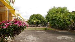 A paved courtyard with a yellow building on one side and a large tree on the other. - Flic En Flac: Cosy Apartment in a nice setting (Flic en Flac)