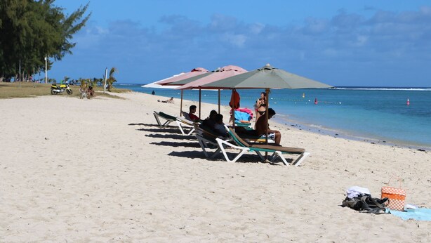 A beach with sun loungers and umbrellas, a clear sky, and the ocean in the background. - Flic En Flac: Cosy Apartment in a nice setting (Flic en Flac)