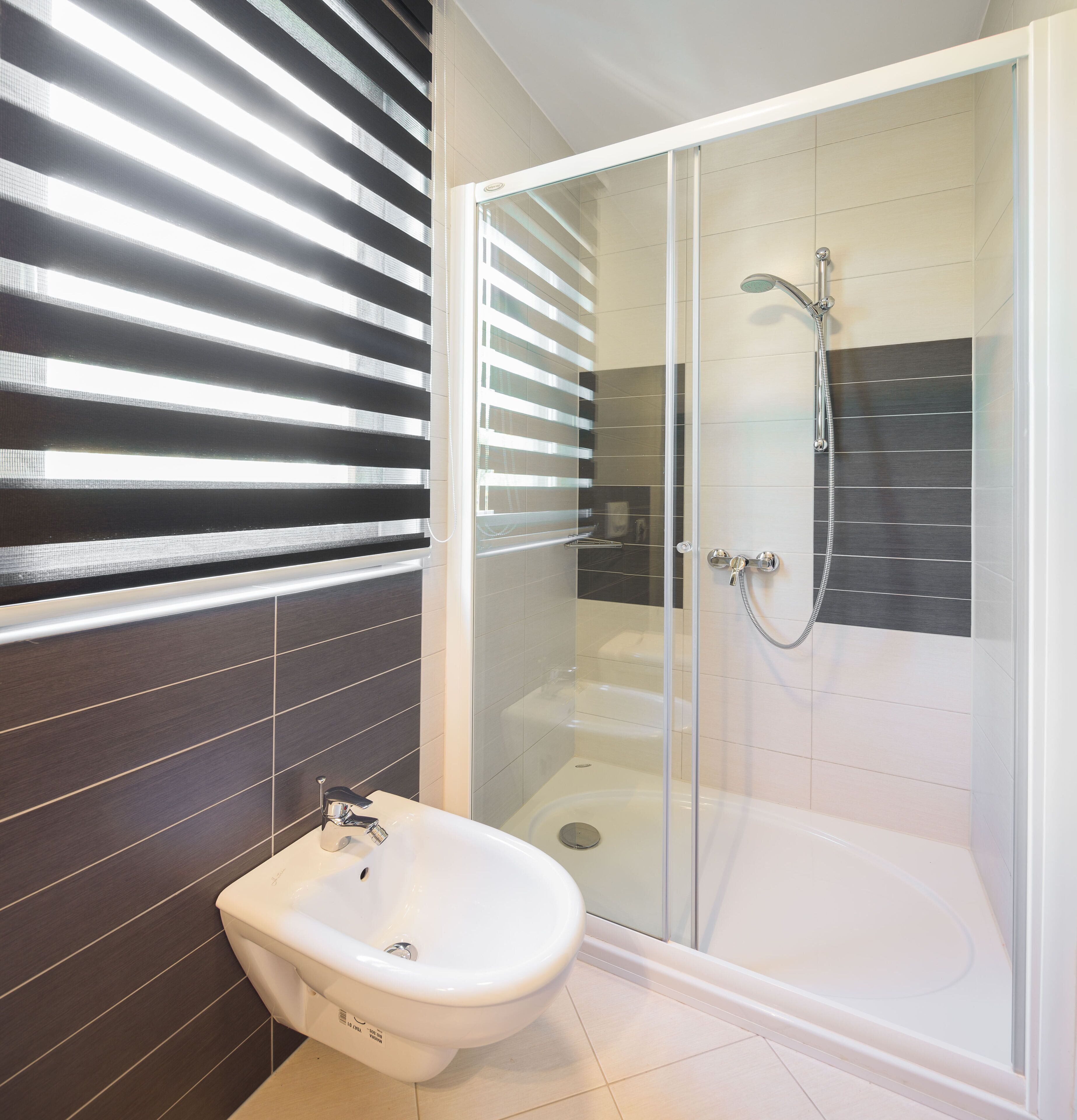 Een moderne badkamer met een douchecabine van glas, een witte wastafel op voet en donkere houten lambrisering aan de muur.
